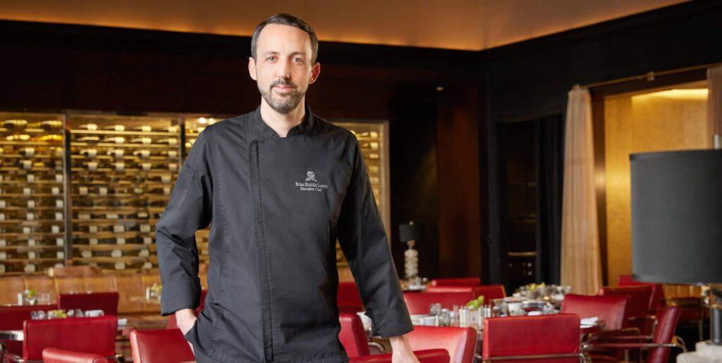 Chef in black dress standing Infront of red chairs